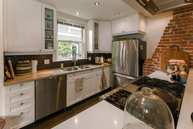 Bright kitchen with white cabinetry, stainless steel appliances, and a brick accent wall. - 4678 West 9th Ave, Vancouver West Side