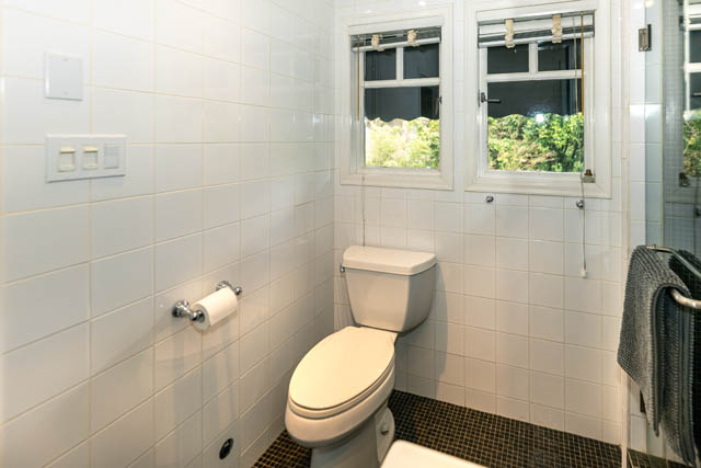 Bright bathroom with white tiles, a toilet, and a window with a view of greenery. - 4678 West 9th Ave, Vancouver West Side