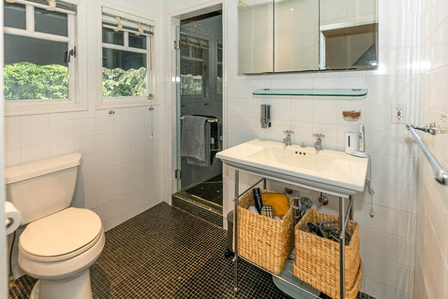 Spacious bathroom with white tile, glass shower, and wicker baskets under the sink. - 4678 West 9th Ave, Vancouver West Side
