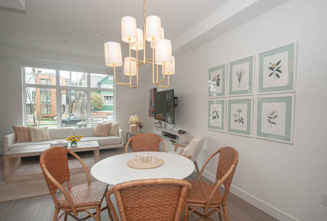 Furnished living and dining area with wicker chairs, white walls, and a city view through large windows. - 211 - 733 E 3rd St, North Vancouver
