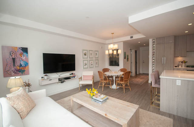 Furnished living room with white walls, modern chandelier, and hardwood floors. - 211 - 733 E 3rd St, North Vancouver