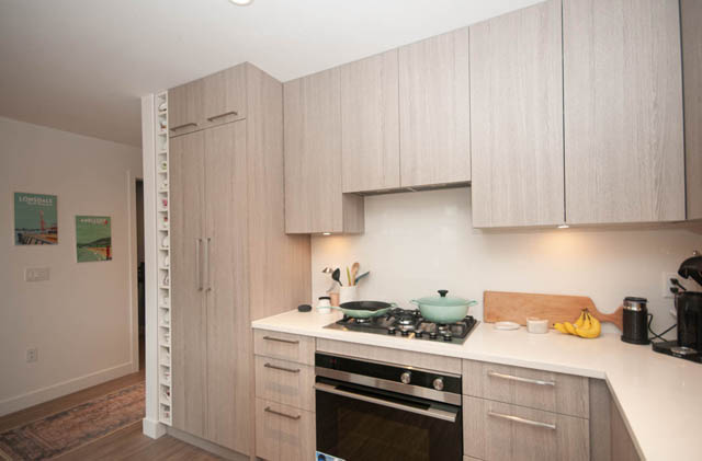 Furnished kitchen with light wood cabinets, modern appliances, and hardwood floors. - 211 - 733 E 3rd St, North Vancouver