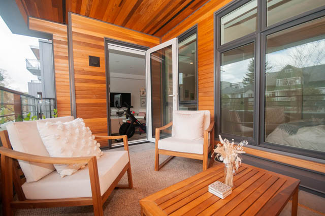 Furnished patio with wooden furniture and large windows, offering a view of the neighborhood. - 211 - 733 E 3rd St, North Vancouver