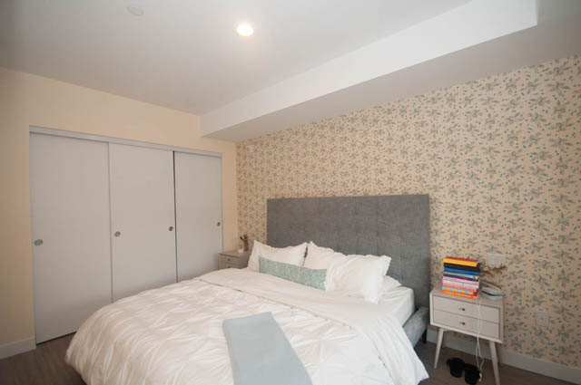 Furnished 1-bedroom + den with floral wallpaper and a neatly made bed. - 211 - 733 E 3rd St, North Vancouver