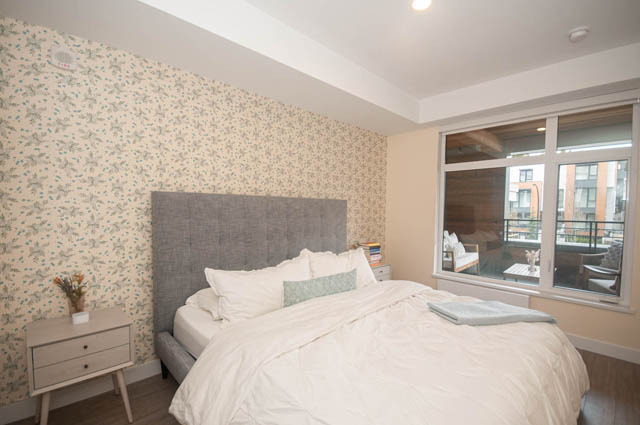 Spacious bedroom with floral wallpaper, large window, and city view. - 211 - 733 E 3rd St, North Vancouver