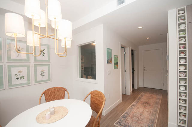 Furnished dining area with white walls, modern chandelier, and hardwood floors. - 211 - 733 E 3rd St, North Vancouver