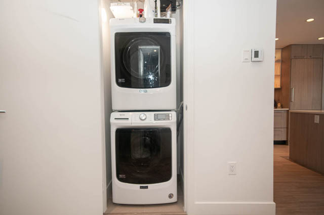 Bright laundry room with stacked washer and dryer, modern cabinetry, hardwood floors. - 211 - 733 E 3rd St, North Vancouver