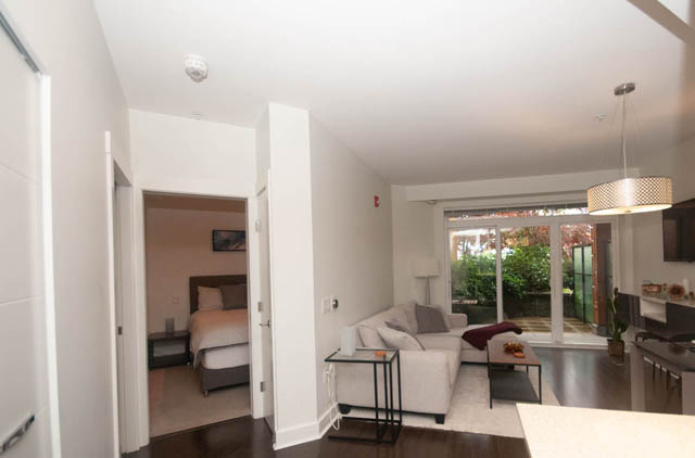 Bright kitchen with white countertops and hardwood floors, leading to a cozy den with a bed and a view of the garden.