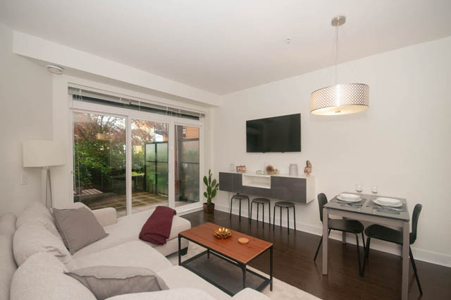 Spacious living room with modern decor, large window, and cozy sofa. - 211 - 733 West 14th, North Vancouver
