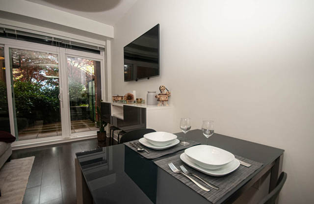 Furnished dining area with modern decor, black table, white plates, and sliding glass door leading to patio. - 211 - 733 West 14th, North Vancouver