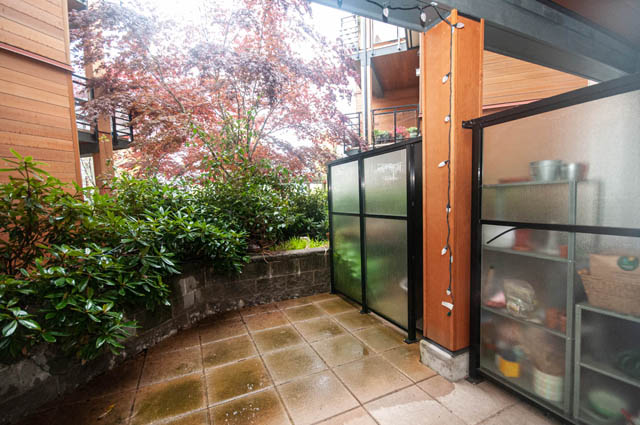 Furnished patio with wooden walls, greenery, and tiled flooring. - 211 - 733 West 14th, North Vancouver