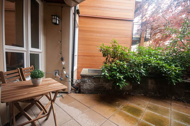Furnished patio with wooden furniture, greenery, and tiled flooring. - 211 - 733 West 14th, North Vancouver
