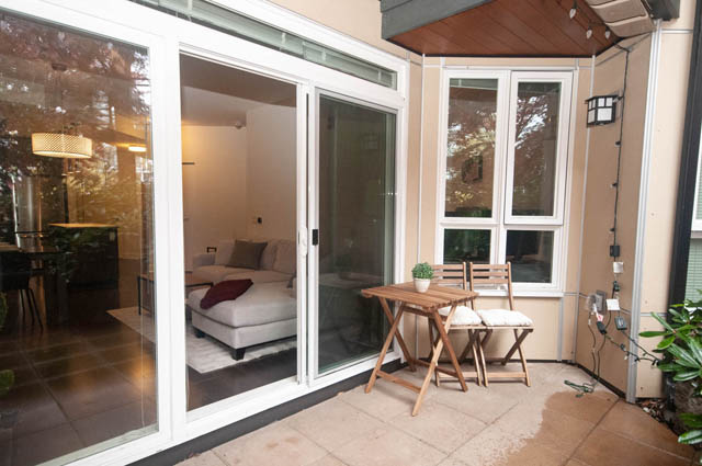 Furnished living room with sliding glass doors, hardwood floors, and a cozy corner setup. - 211 - 733 West 14th, North Vancouver