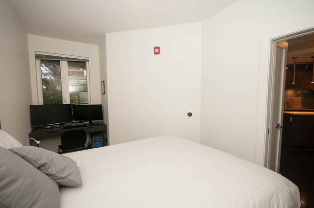 Bright bedroom with white walls, built-in desk, and partial view of kitchen countertop. - 211 - 733 West 14th, North Vancouver