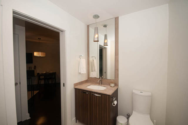 Furnished 1-bedroom + den with hardwood floors and a modern bathroom featuring a large mirror and pendant lights.