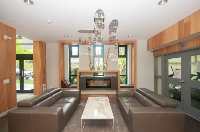 Spacious living room with modern furniture, large windows, and wooden accents. - 211 - 733 West 14th, North Vancouver
