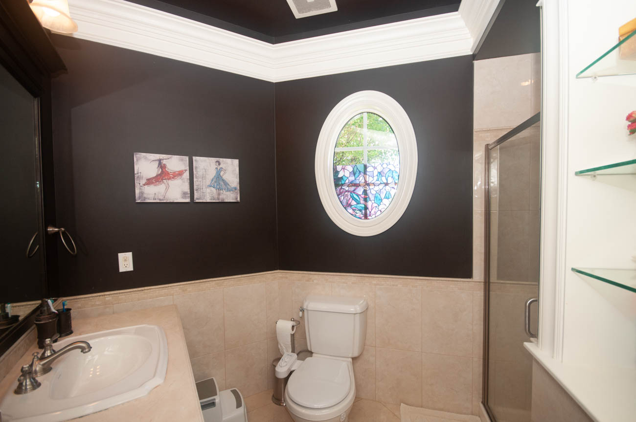 Bright bathroom with dark walls, oval window, and beige tiled floor. - 3440 Wellington Crescent, North Vancouver