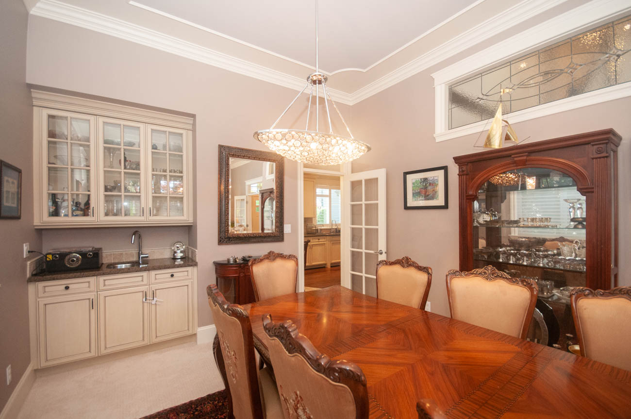 Furnished dining room with hardwood floors and ornate chandelier, leading to a kitchen with granite countertops.