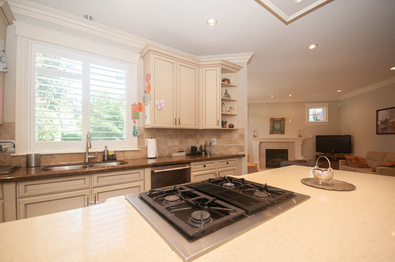 Bright kitchen with granite countertops and a large island, leading into a living area with a fireplace. - 3440 Wellington Crescent, North Vancouver
