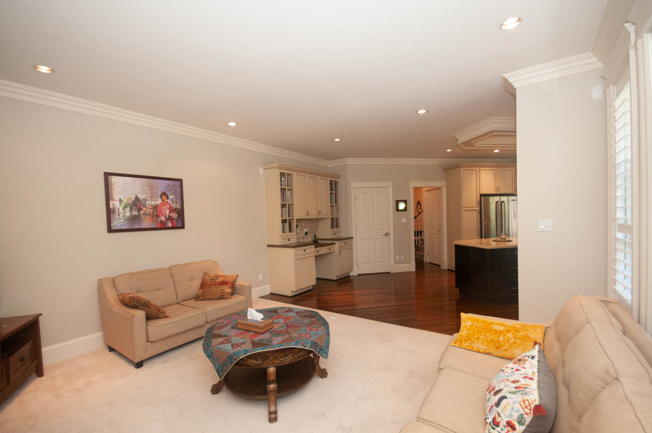 Bright living room with hardwood floors, beige furniture, and a kitchen in the background. - 3440 Wellington Crescent, North Vancouver