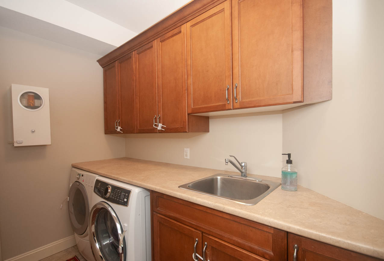 Bright laundry room with granite countertops and wooden cabinets. - 3440 Wellington Crescent, North Vancouver