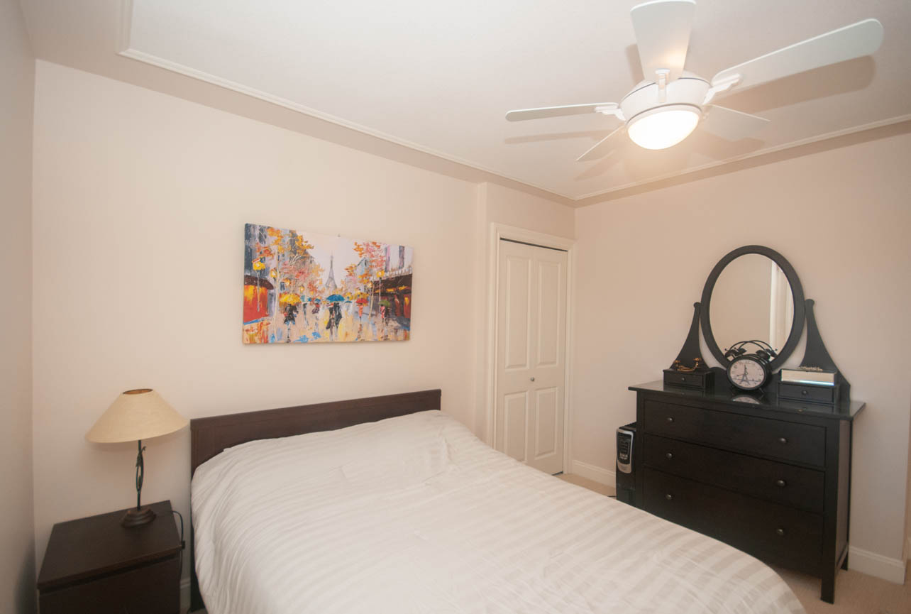 Furnished bedroom with two twin beds, dark wood furniture, and a colorful cityscape painting. - 3440 Wellington Crescent, North Vancouver