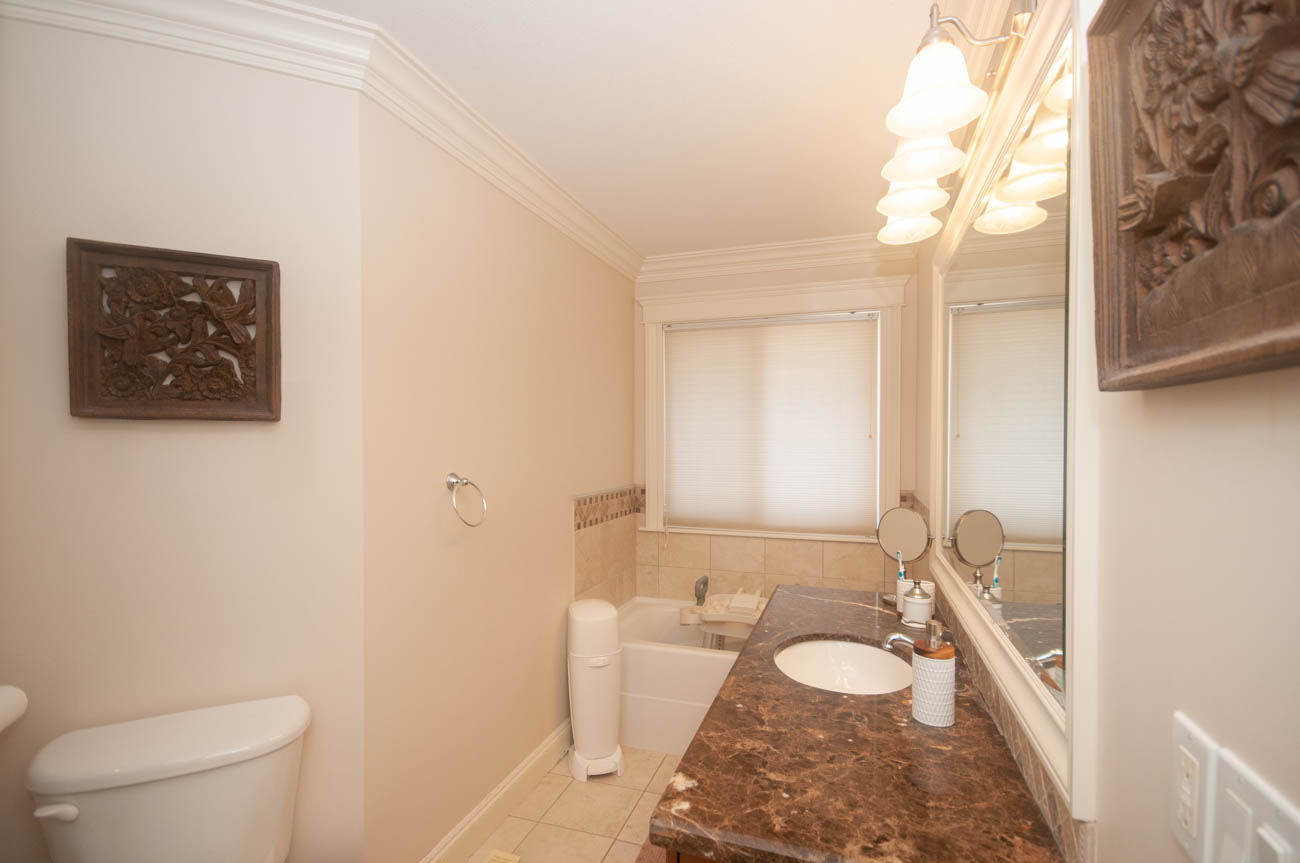 Bright bathroom with marble countertop and window with blinds. - 3440 Wellington Crescent, North Vancouver