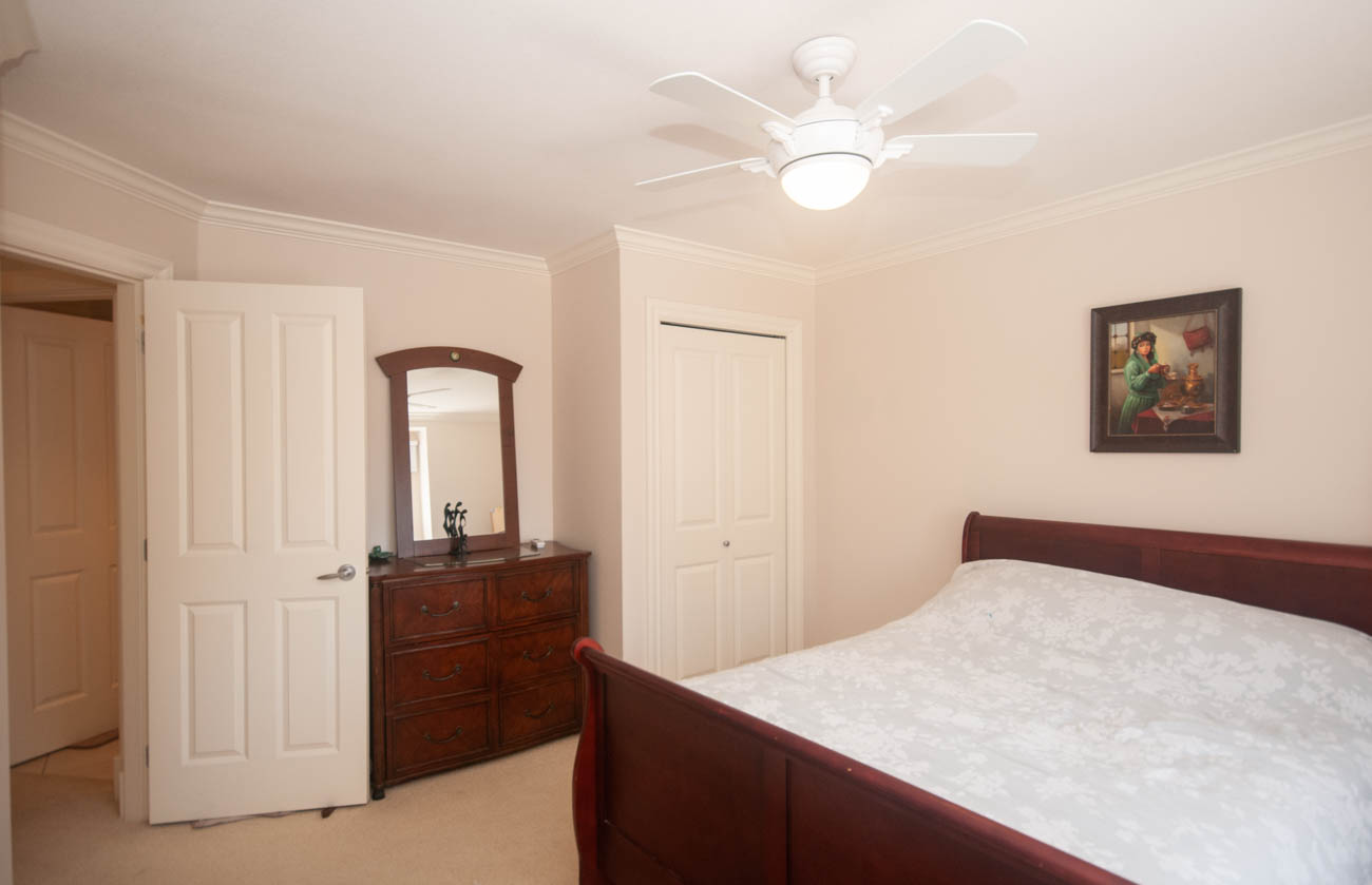 Furnished bedroom with wooden furniture, white door, and ceiling fan. - 3440 Wellington Crescent, North Vancouver