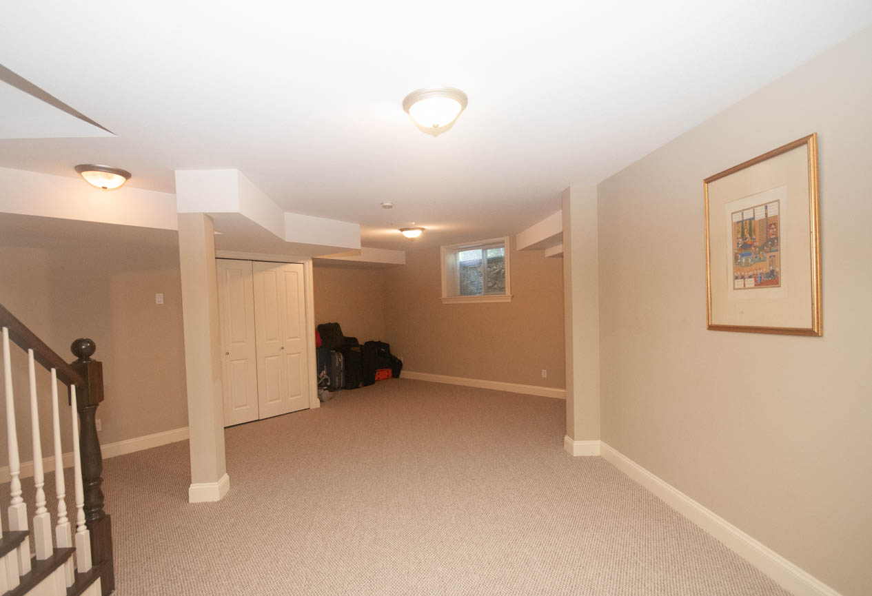 Spacious basement with carpeted flooring, exposed beams, and a framed picture on the wall. - 3440 Wellington Crescent, North Vancouver