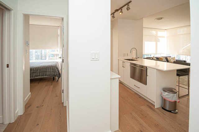 The kitchen has stainless steel appliances, hardwood floors, track lighting, and a city view visible from the adjacent bedroo