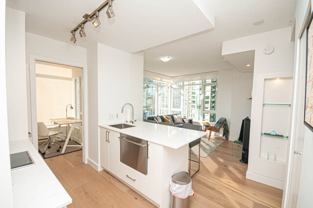 The kitchen features a white island with a sink, stainless steel appliances, hardwood floors, track lighting, and an open vie