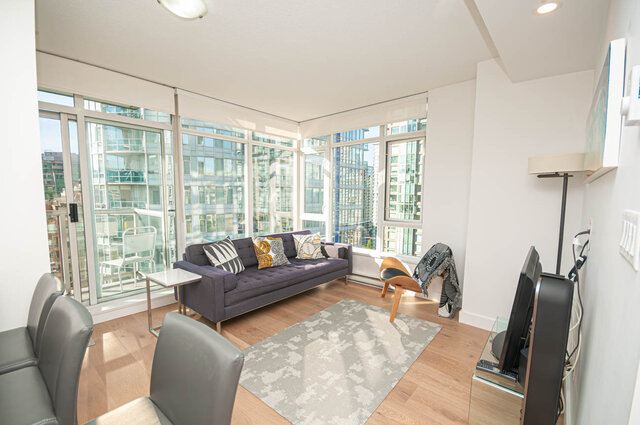 The living room contains a sofa with throw pillows, multiple chairs, a television on a stand, hardwood flooring, floor-to-cei