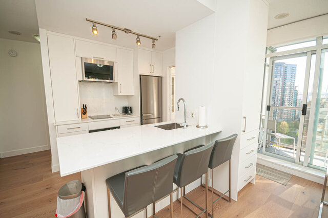 The kitchen features white cabinets, stainless steel appliances, an island with a sink, hardwood floors, and floor-to-ceiling