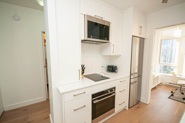 This is a kitchen with white cabinets, stainless steel microwave, refrigerator, oven, stovetop, and hardwood floors.