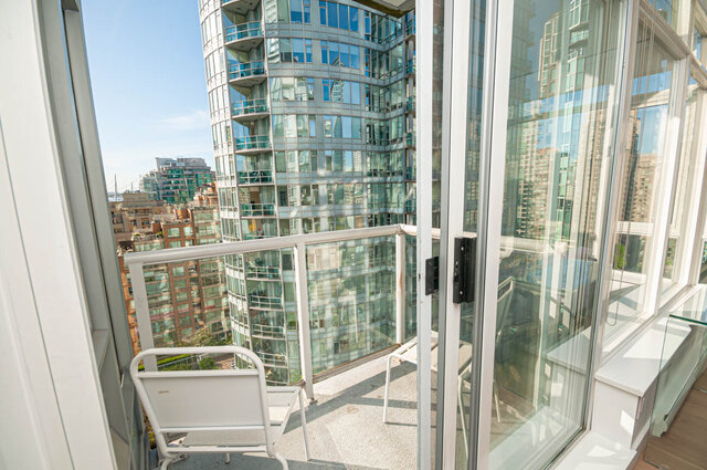 The balcony has a metal railing, two white chairs, and a view of high-rise buildings. - 1306-480 Robson Street, Vancouver Downtown