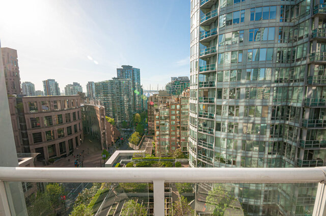 The balcony has a railing with a city view of tall buildings and greenery under a clear blue sky. - 1306-480 Robson Street, Vancouver Downtown