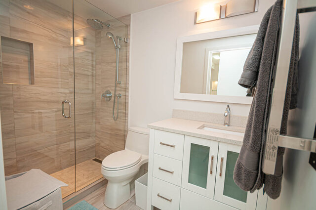 This bathroom features a glass-enclosed shower, a white toilet, and a vanity with a sink and mirror. - 1306-480 Robson Street, Vancouver Downtown