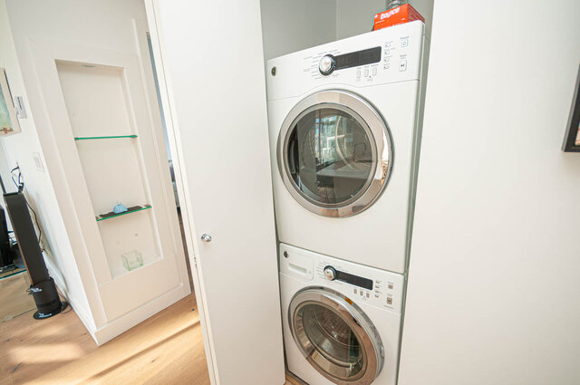 Laundry room with stacked washer and dryer, hardwood floors, and a red box on top of the dryer. - 1306-480 Robson Street, Vancouver Downtown
