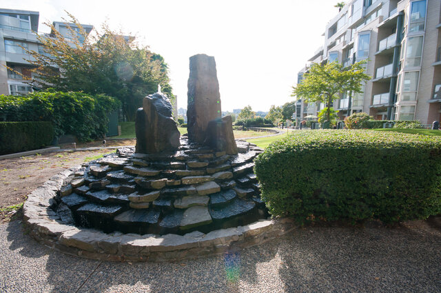 building exterior featuring a stone structure, paved walkway, apartment buildings, and landscaped greenery