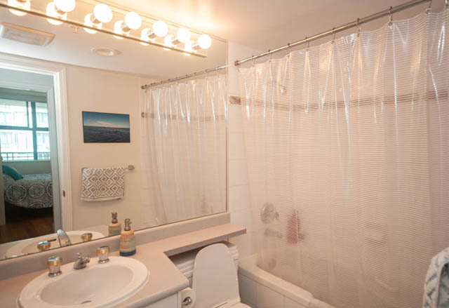 Bathroom with white sink, toilet, and shower curtain, featuring a city view in the mirror. - 801-1128 Quebec st, Vancouver Downtown