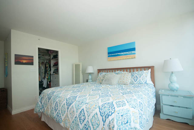 Spacious bedroom with wooden floors, blue patterned bedding, and beach-themed artwork. - 801-1128 Quebec st, Vancouver Downtown