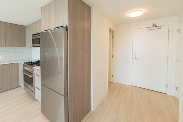 Modern kitchen with sleek countertops and hardwood floors, featuring a stainless steel refrigerator and gas stove.