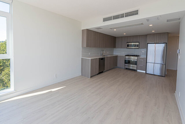 Open-concept living space with hardwood floors and modern kitchen featuring stainless steel appliances and light wood...