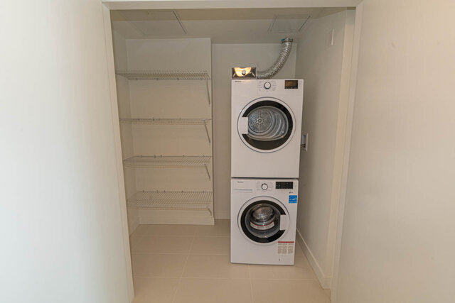 Compact laundry room with white shelves and a stacked washer and dryer. - 1105 - 1401 Hunter Street, North Vancouver