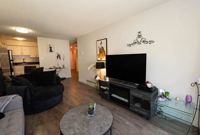 Furnished living room with hardwood floors and a modern TV setup. - 306 - 212 Forbes Ave, North Vancouver