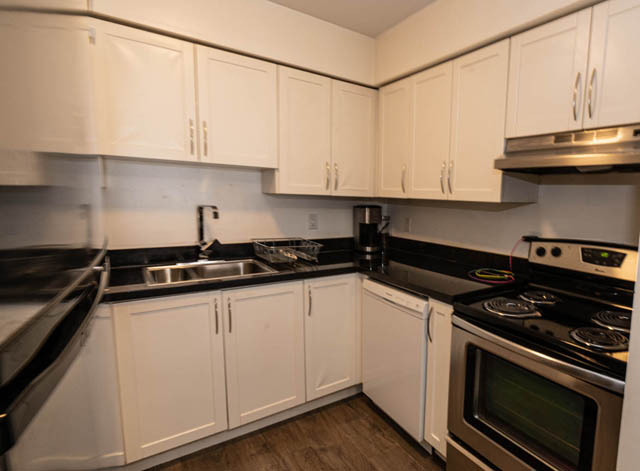 Bright kitchen with white cabinets, stainless steel appliances, and hardwood floors. - 306 - 212 Forbes Ave, North Vancouver
