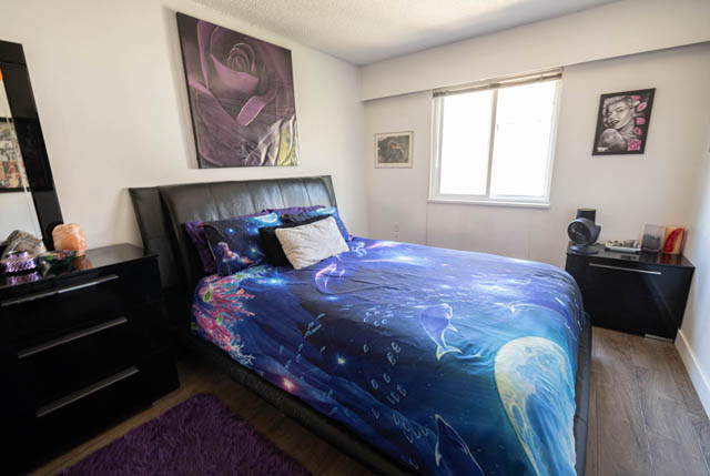 Furnished 1-bedroom condo with a cozy bed, colorful bedding, and a large window letting in natural light. - 306 - 212 Forbes Ave, North Vancouver