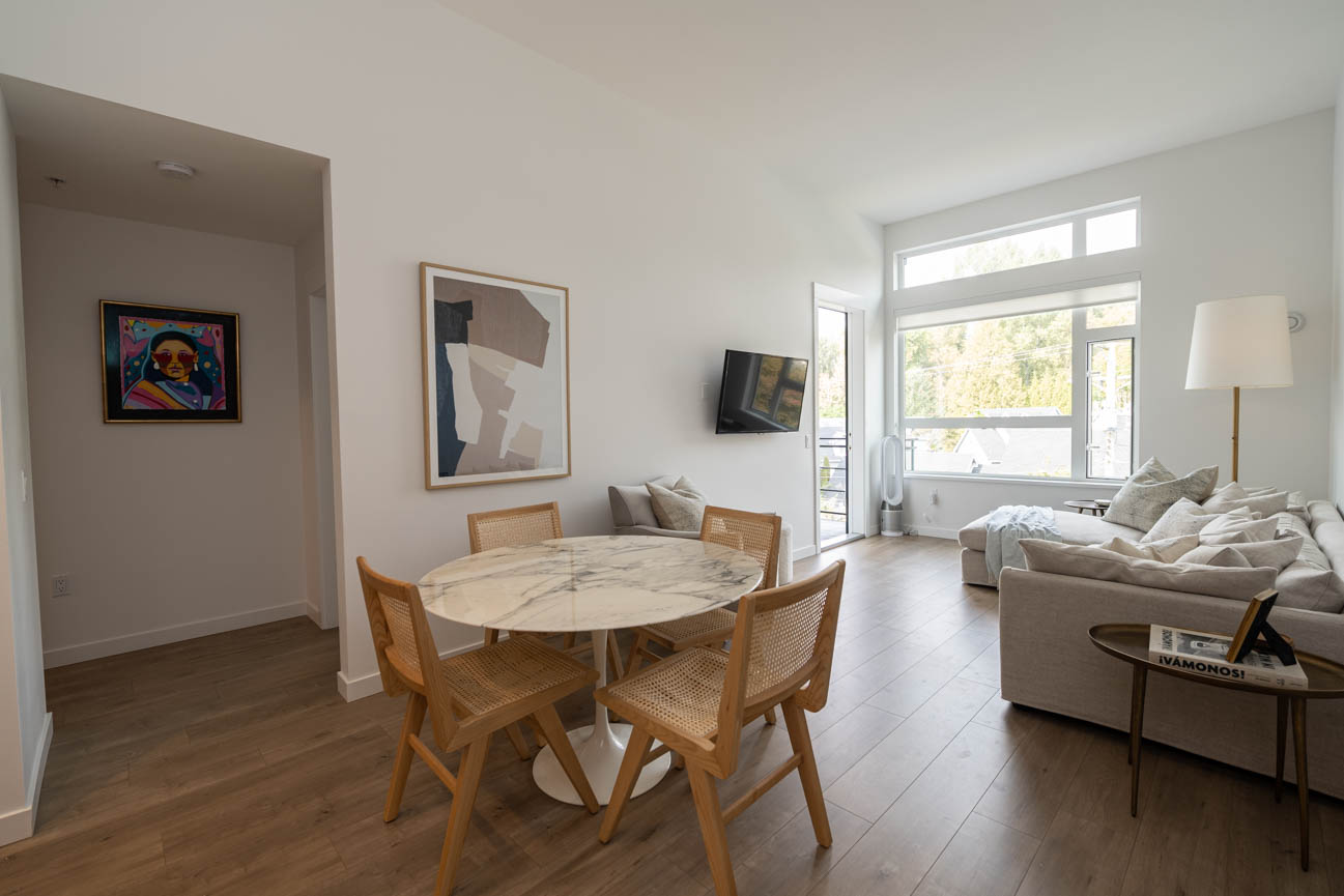 Bright dining area with marble table and modern chairs, leading to a cozy living room with large windows and a...