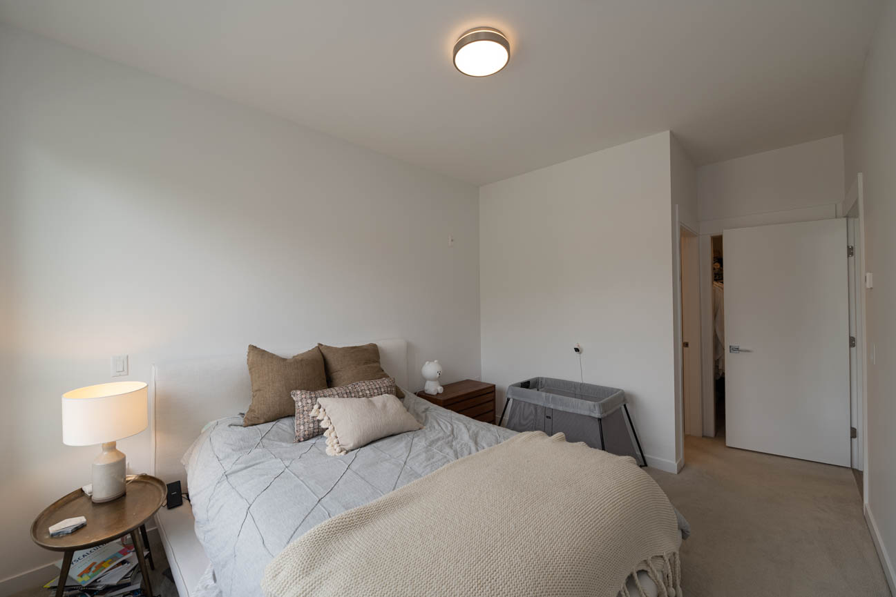 Furnished bedroom with cozy bedding and a small bedside table, hardwood floors visible. - 308 - 715 W15th Street, North Vancouver
