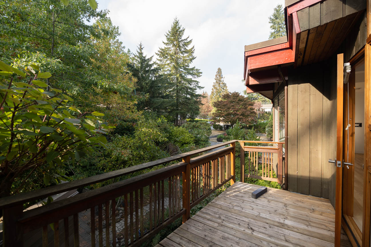 Furnished balcony with wooden railings and lush greenery, leading to a shared house. - Upper - 3248 Robinson Road, North Vancouver